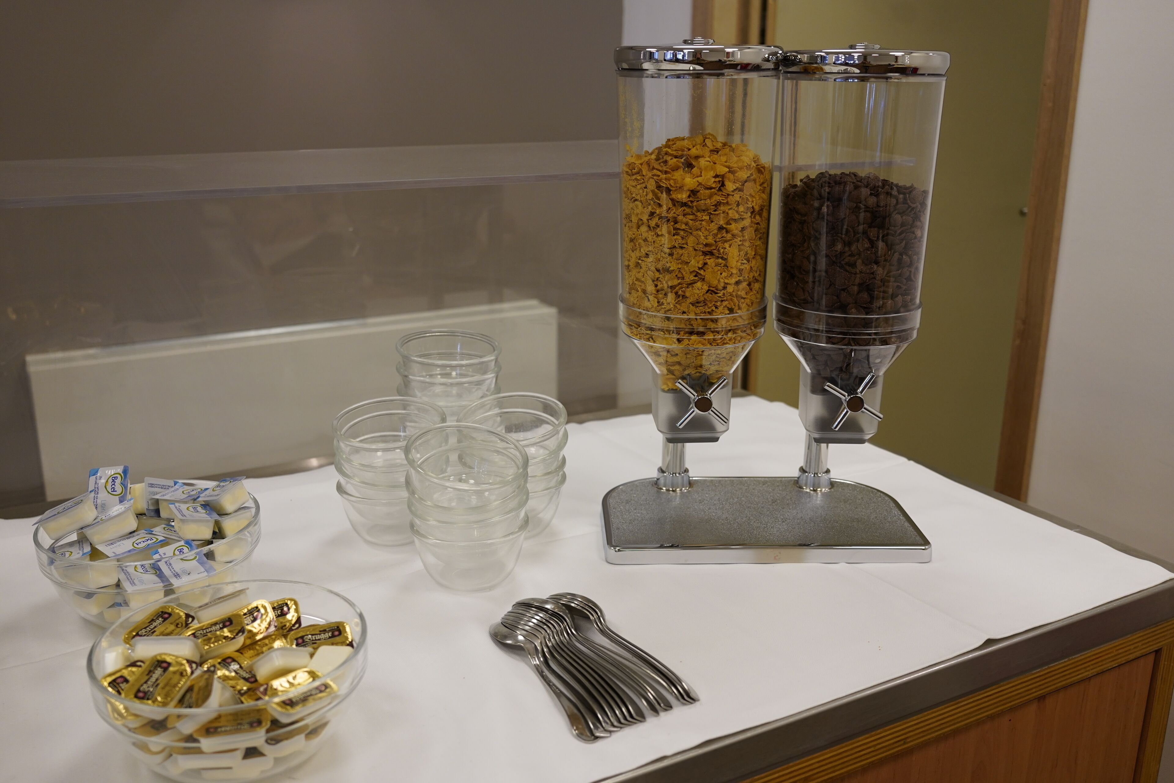 Ein Buffet mit durchsichtigen Glasbehältern für Müsli und Kaffee, Plastikbechern und Schalen mit Snacks.