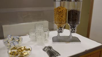 Ein Buffet mit durchsichtigen Glasbehältern für Müsli und Kaffee, Plastikbechern und Schalen mit Snacks.