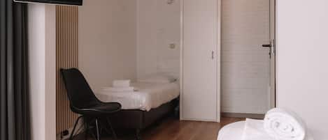 A hotel room with a bed, a chair, a TV, and a wardrobe.