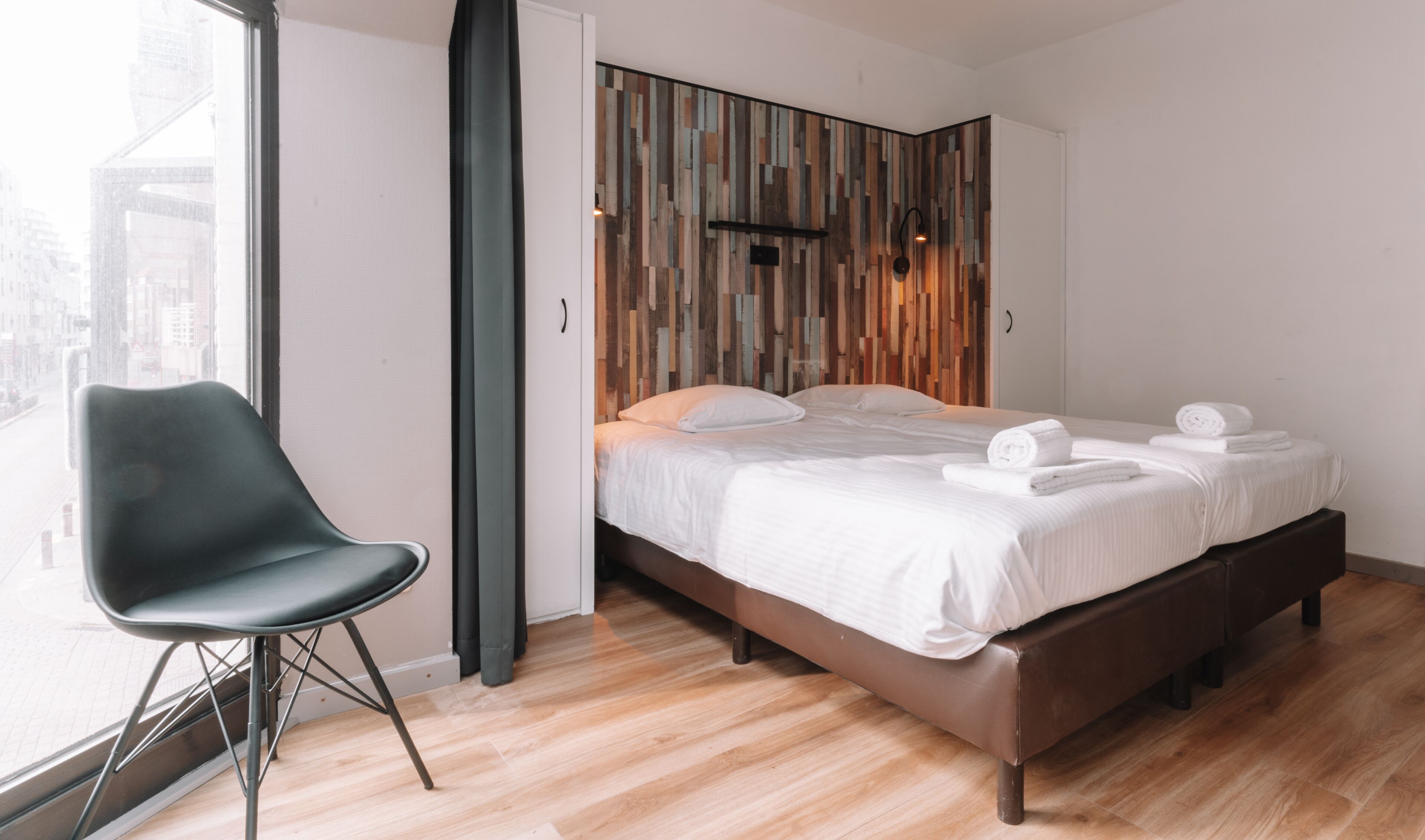 Et moderne hotelværelse med seng, stol og udsigt over byen gennem vinduet.