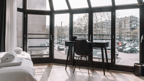Una habitación de hotel con un gran ventanal, una cama con toallas dobladas, un escritorio y una silla.