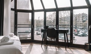 Una habitación de hotel con un gran ventanal, una cama con toallas dobladas, un escritorio y una silla.