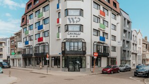 Un hotel de varios pisos con un diseño de esquina distintivo, que presenta una combinación de fachadas blancas y marrones, varios balcones y un llamativo letrero 'Cavalli'.