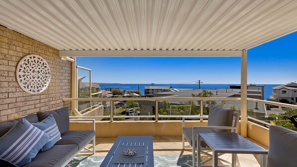 Un balcón con vista al mar, un sofá, una mesa y un adorno de pared.