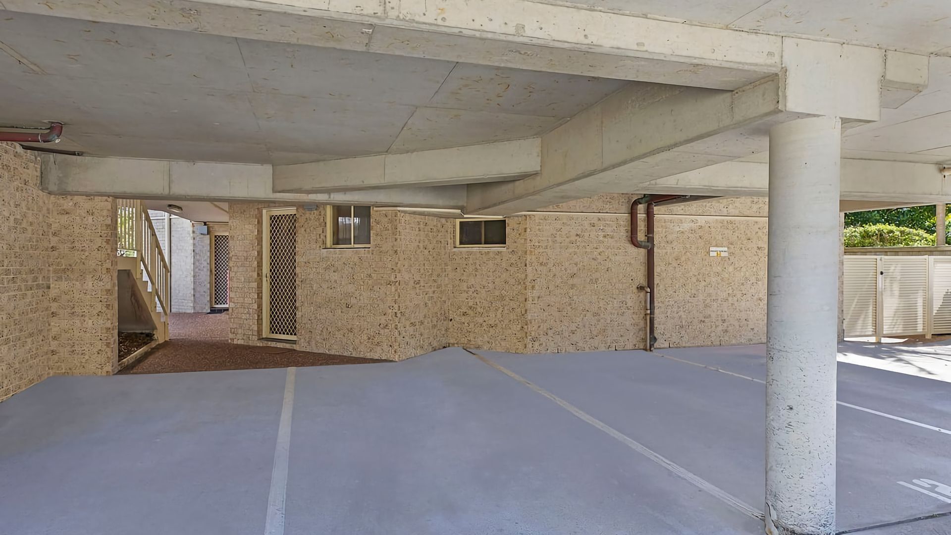 An empty parking garage with concrete pillars, a flat roof, and a brick wall.