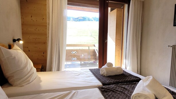A bedroom with two beds, a wooden ceiling, a window with curtains, and a view of the outside. - Renovated 3-star apartment in Les Gets, at the slopes, parking and wifi inclusive, for 8 pax (Les Gets)