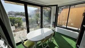A balcony with a white table and chairs, green artificial grass, and a view of buildings and parked cars. - Calm 2BR with terrace, AC and parking near beach (Saint-Cyprien)