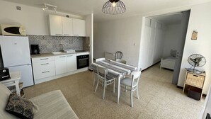 A compact kitchen with white cabinets, a dining table with chairs, a microwave, and a kettle.