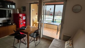 Et lille værelse med tekøkken, spisebord med stole, en lille sofa og en skydedør til en udendørs balkon.