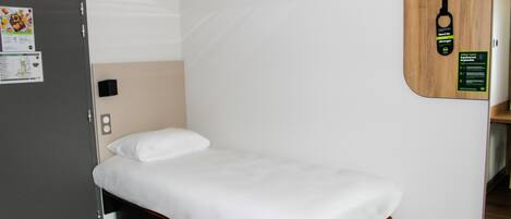 A single bed with a white mattress and a wooden headboard, a gray door, and a wall-mounted wooden panel with a hanging keychain.