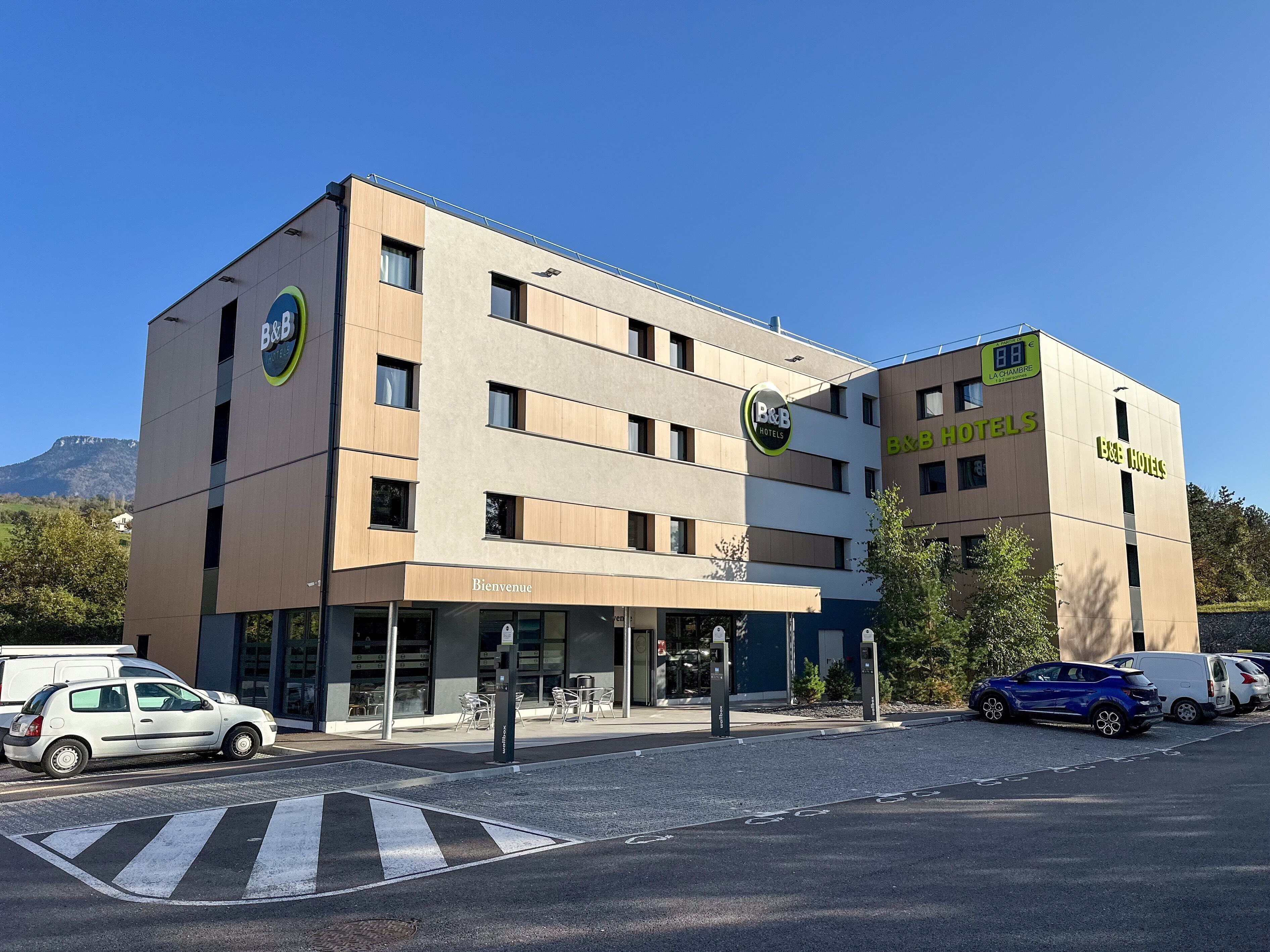 A B&B hotel with a 'Bienvenue' sign, outdoor seating, and a parking area.