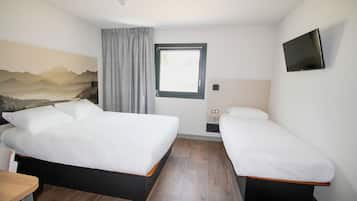 Ein Hotelzimmer mit zwei Betten, einem Schreibtisch, einem Fernseher und einem Fenster mit Vorhängen.