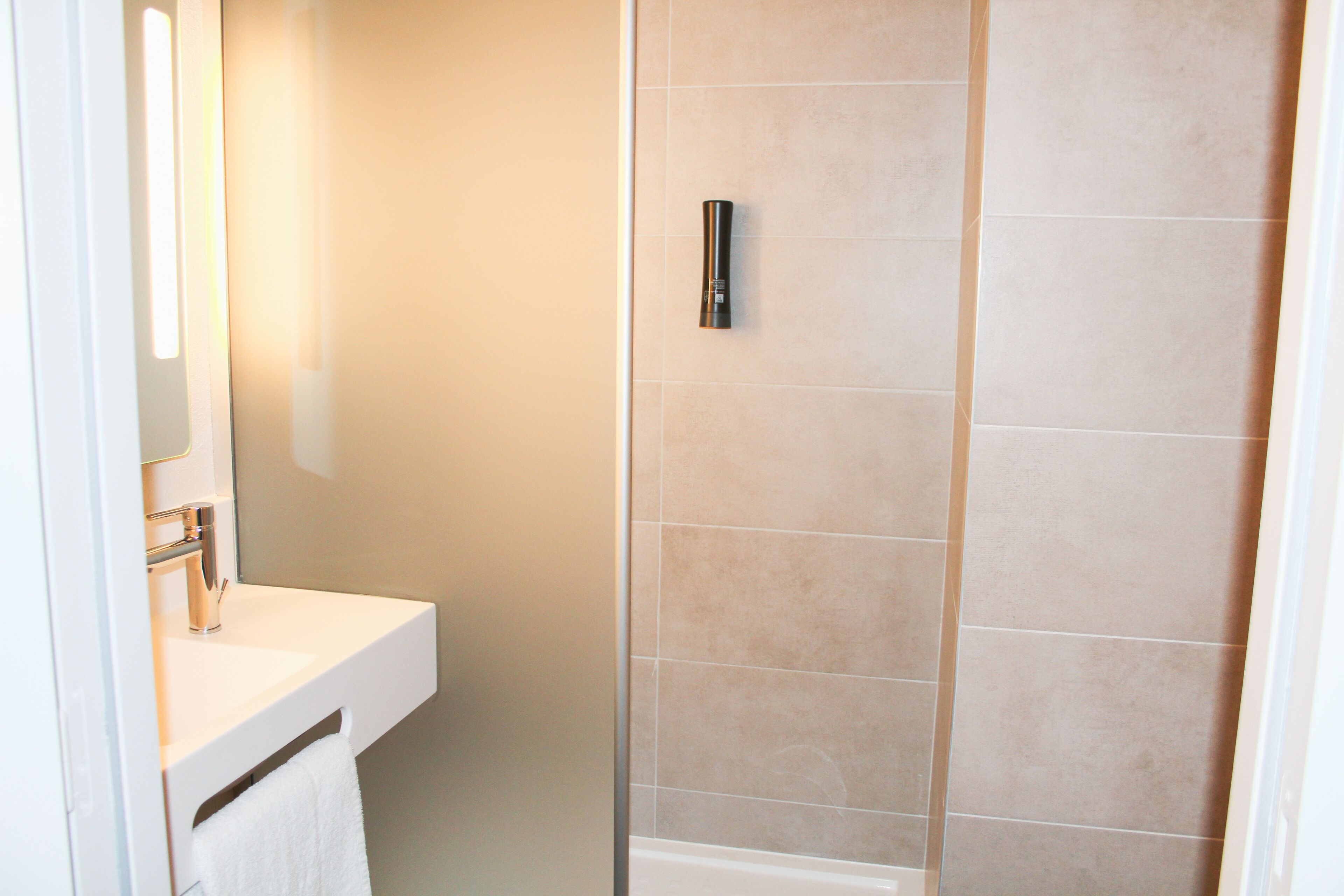 A bathroom with a white sink, a mirror, and a shower with beige tiles.