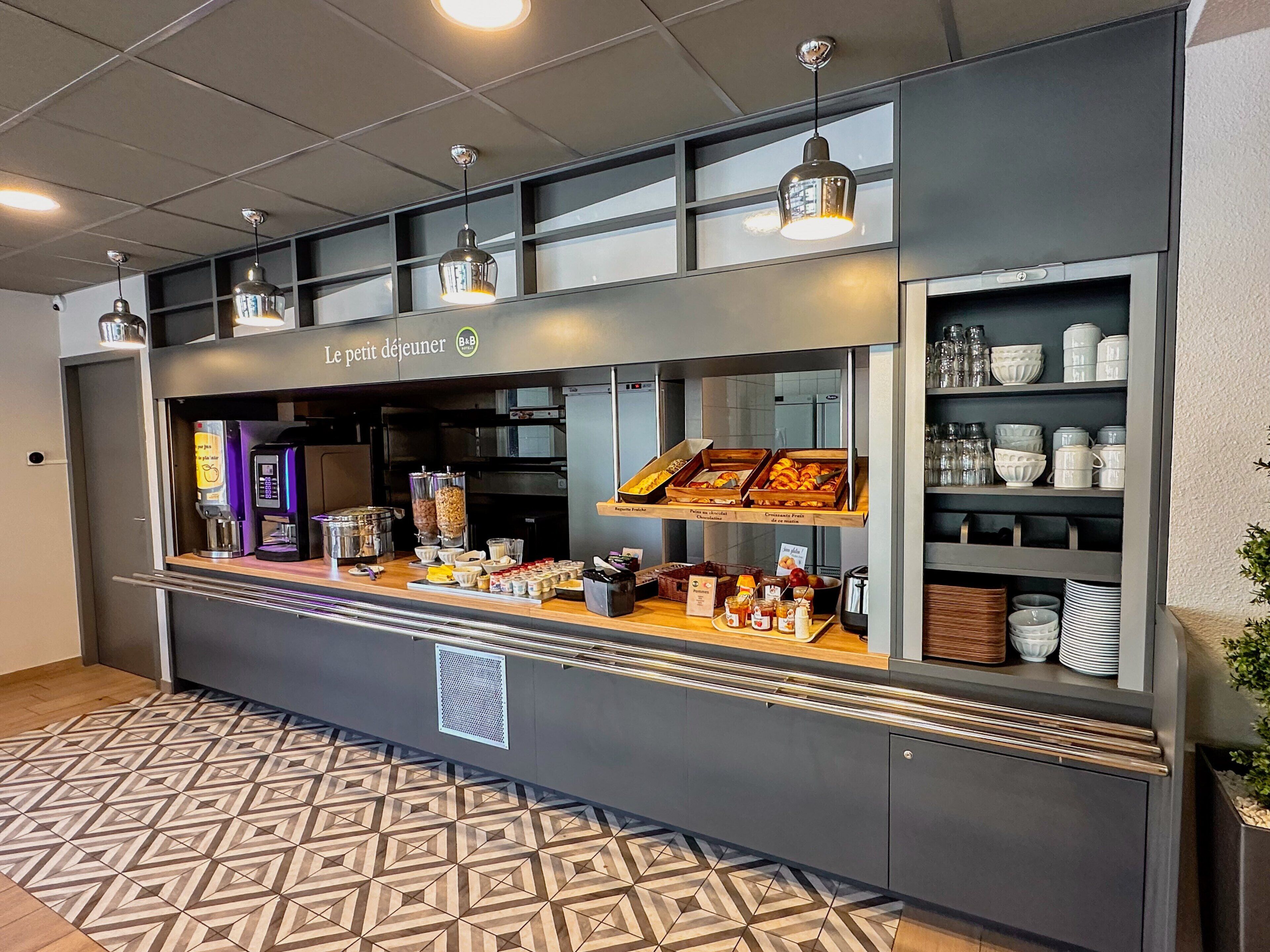 A café with a counter displaying pastries, a coffee machine, and various condiments.
