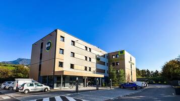A B&B hotel with a modern design, a visible entrance, and a parking area with cars.