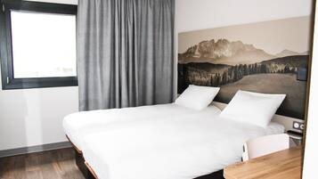 Quarto de hotel com uma cama grande, uma escrivaninha de madeira, uma janela com cortinas e uma pintura da paisagem de montanhas na parede.