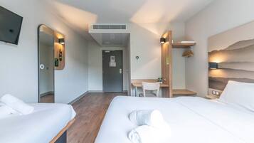 A hotel room with two beds, a desk, a chair, a mirror, and a wall-mounted TV.