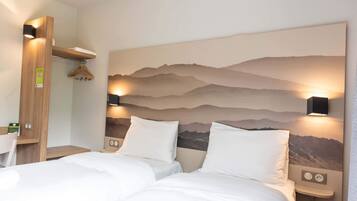 Een hotelkamer met twee bedden, een houten hoofdbord, een aan de muur bevestigde televisie en een berglandschap op de muur.