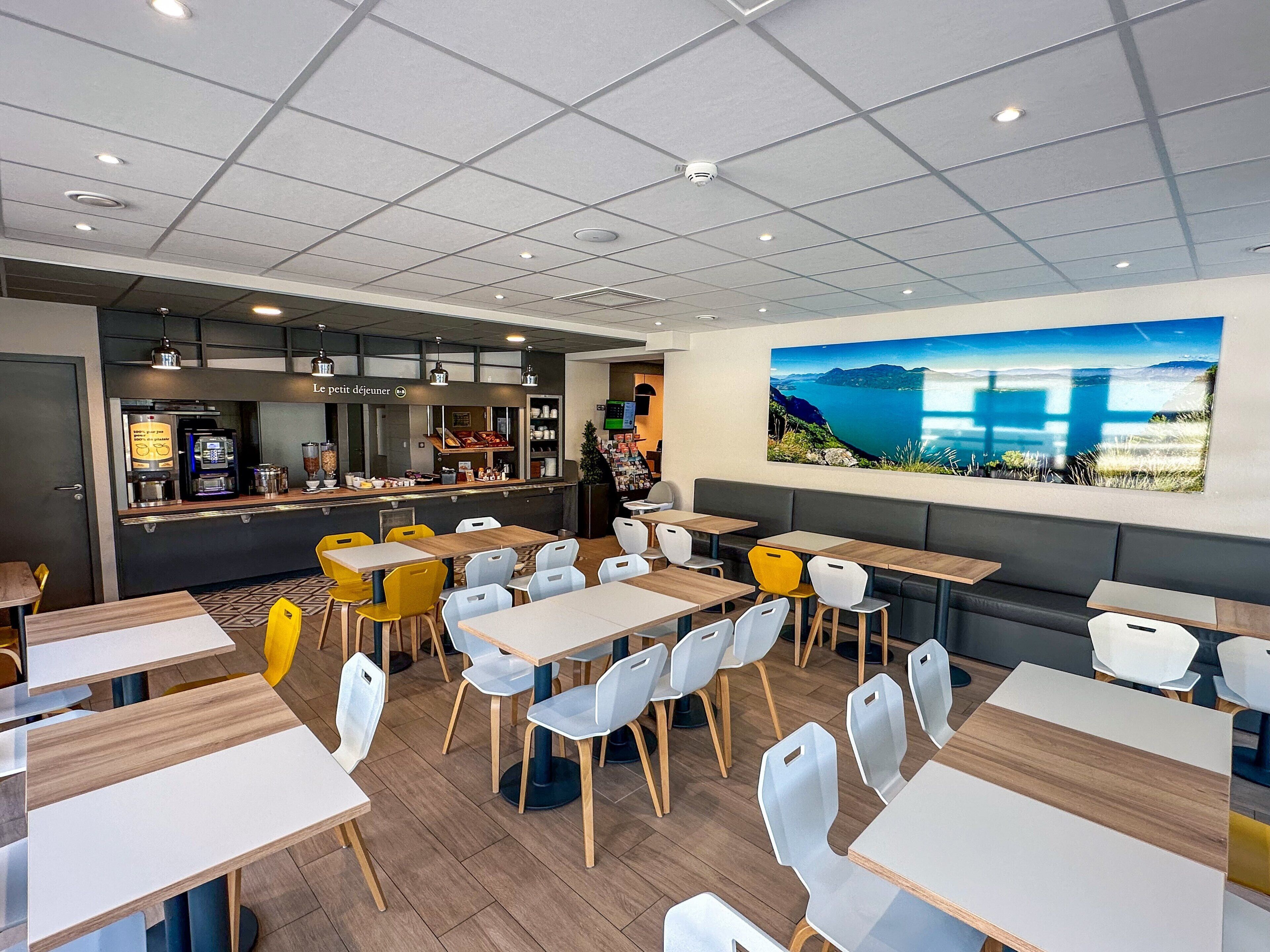 A modern cafe with multiple tables and chairs, a coffee machine, and a large scenic painting on the wall.