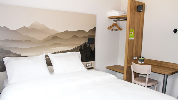 Habitación de hotel con cama, escritorio y silla. En la pared, un cuadro que representa un paisaje montañoso.