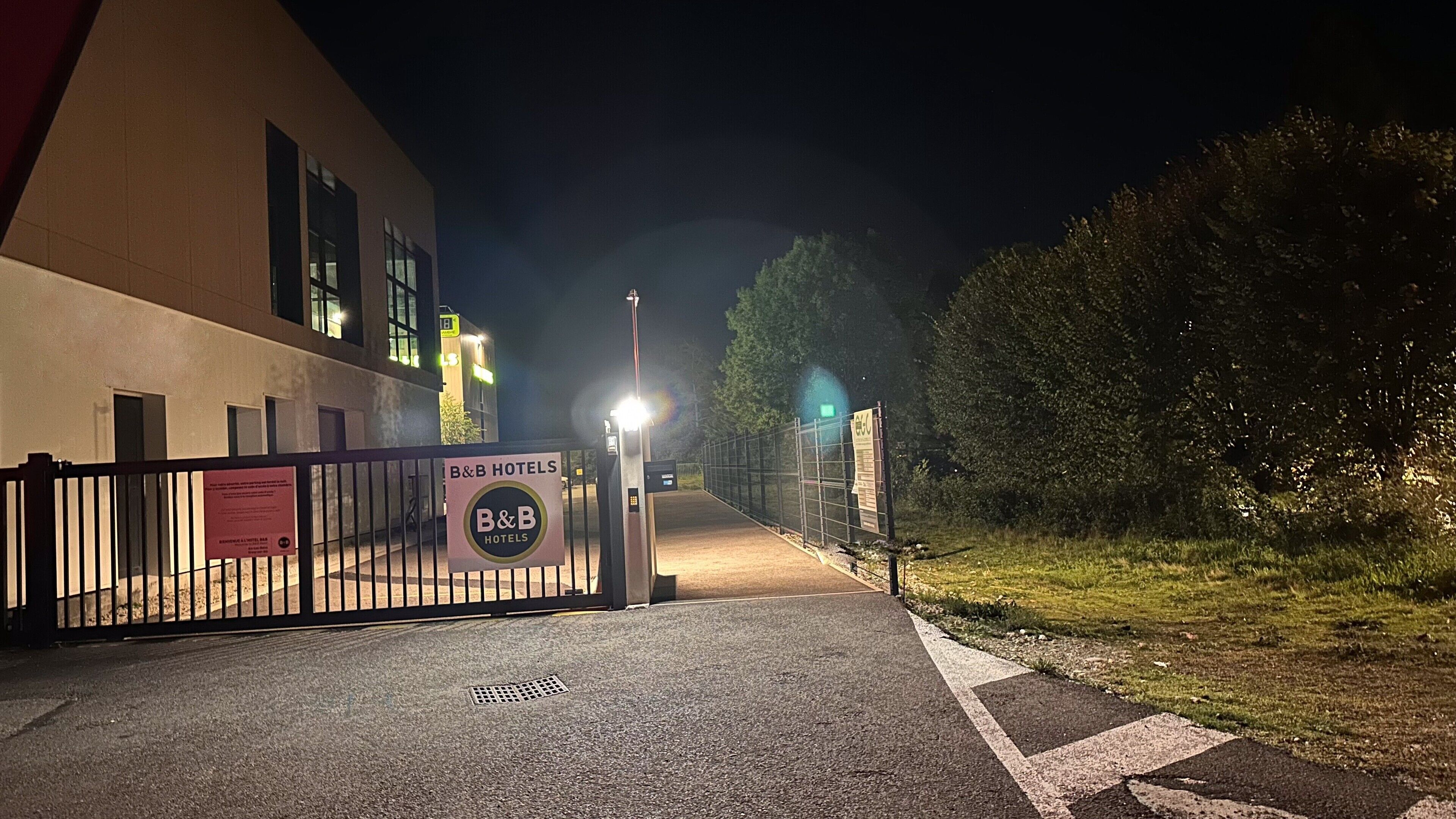 Una entrada tancada amb porta de B&B Hotels de nit, amb un camí ben il·luminat cap a l'edifici.
