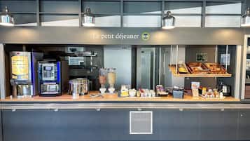 Ein Frühstücksbuffet mit Kaffeeautomaten, einer Obstauslage und einem Schild mit der Aufschrift 'Le petit déjeuner'.