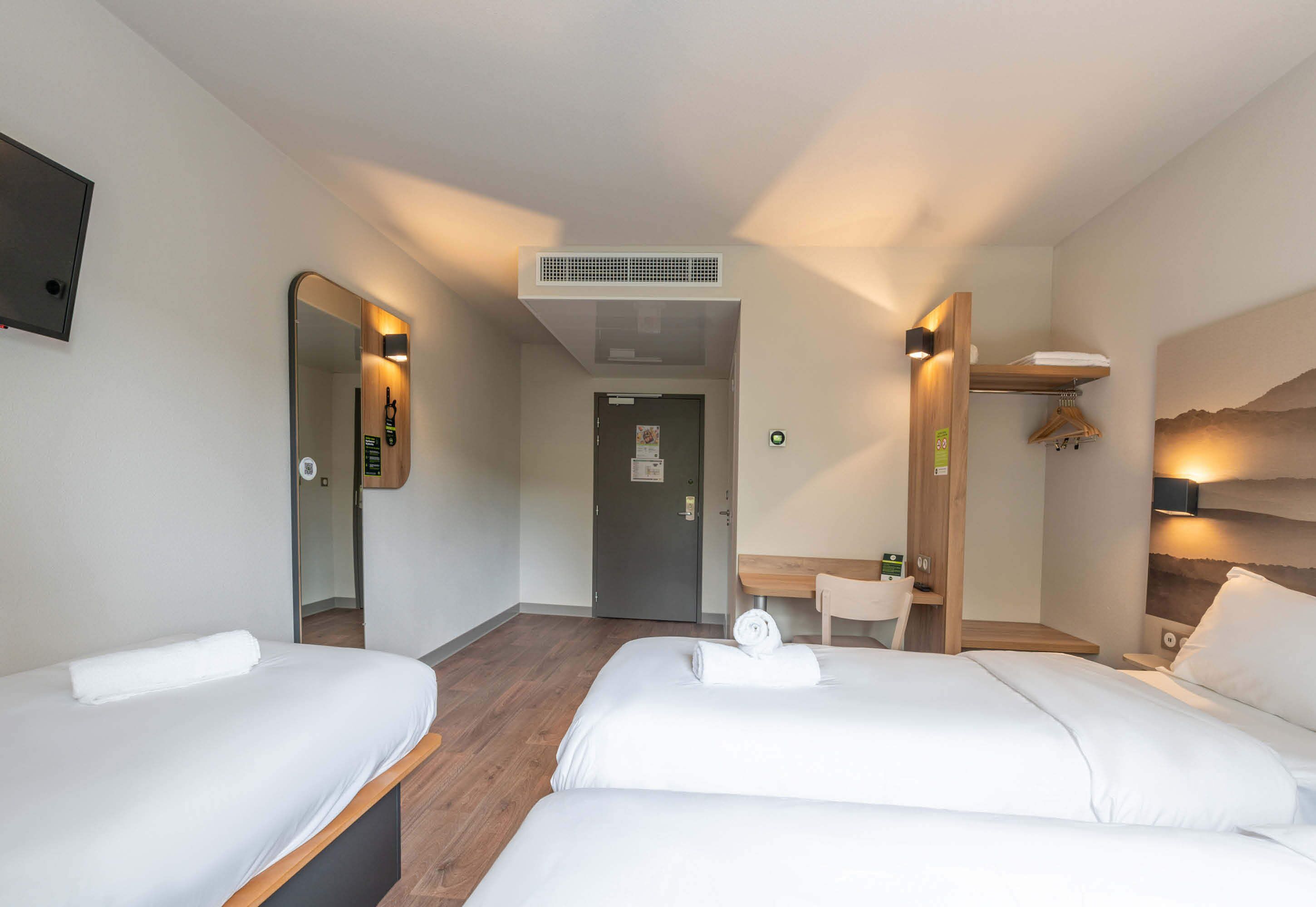 A hotel room with two beds, a desk, a mirror, a small bathroom, and a view of the mountains.