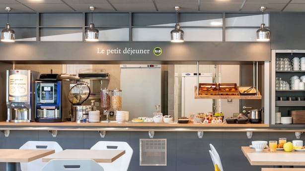Una cafetería con mostrador de autoservicio, zona de mesas y un cartel de menú visible.