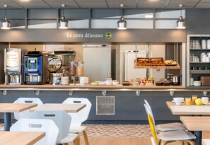 Una cafetería con mostrador de autoservicio, zona de mesas y un cartel de menú visible.
