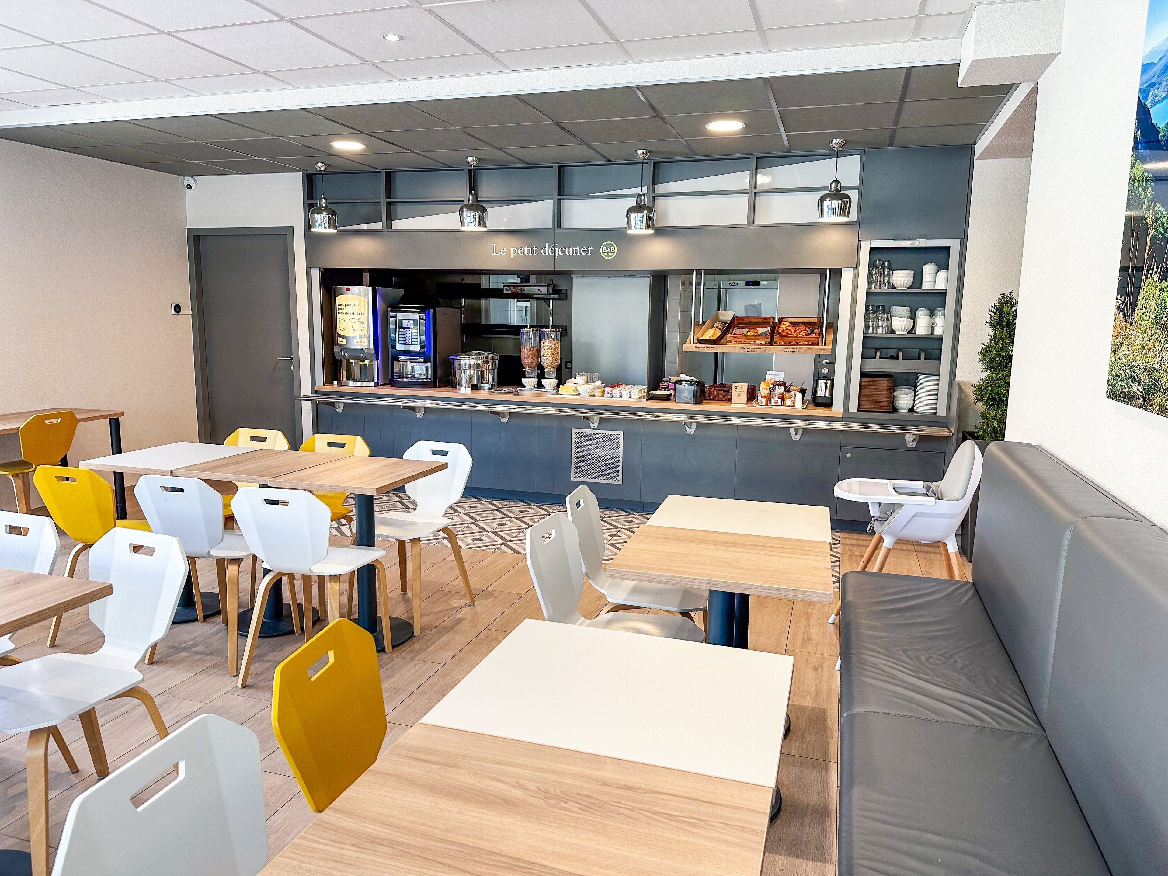 Un café avec des tables et des chaises, un comptoir où sont exposés des produits alimentaires, et une vue sur l’extérieur.