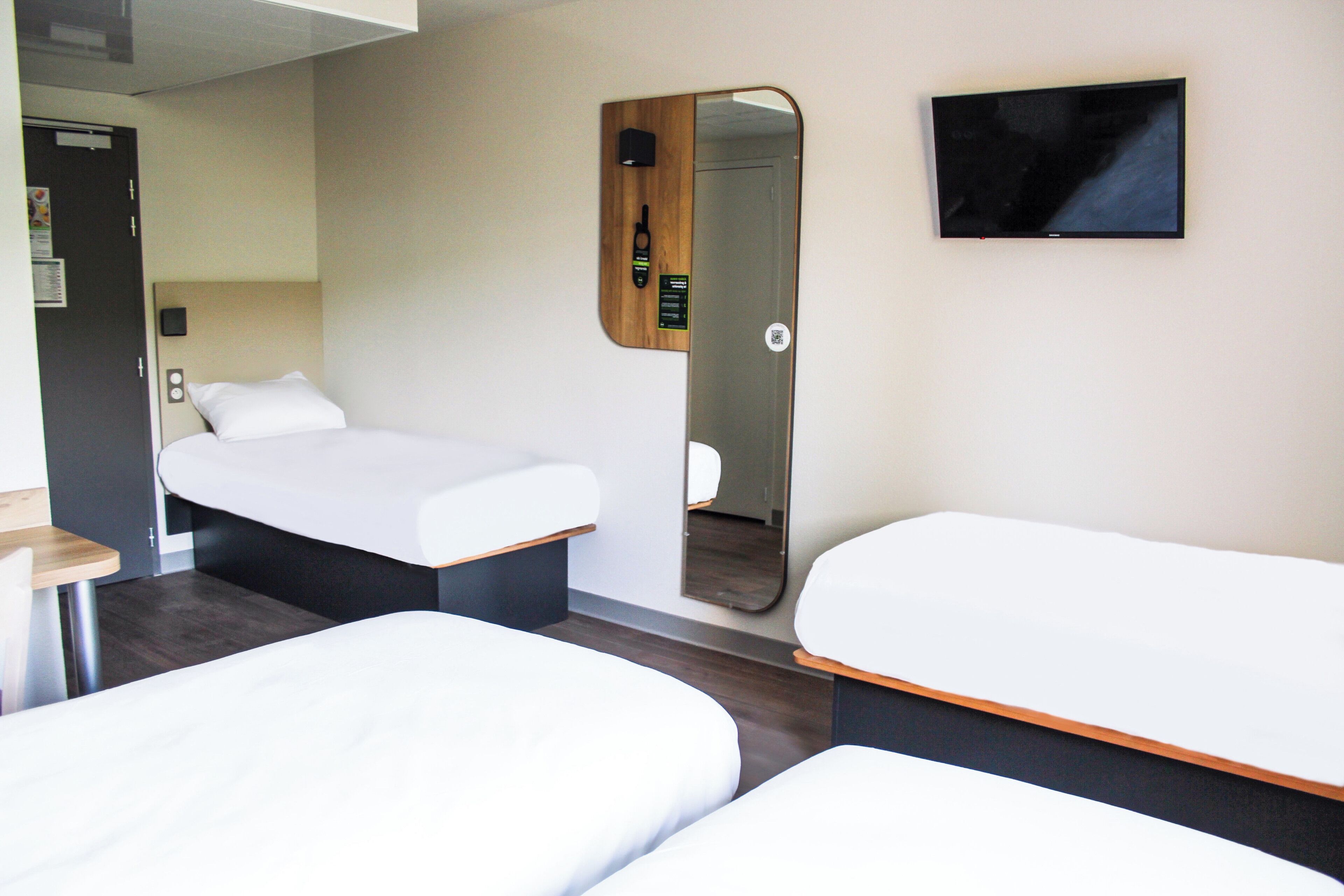 Habitació d'hotel amb dos llits, televisió, mirall, fusta de capçal i taula petita.