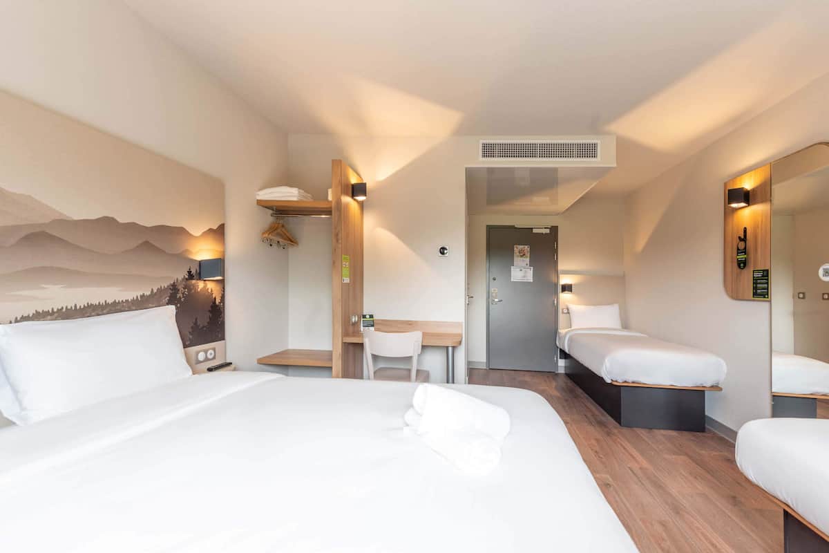 Habitación de hotel con una cama grande, un escritorio y una silla. Se ve una puerta y un espejo en la pared.
