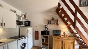 Une cuisine compacte équipée d’un lave-linge, d’un four à micro-ondes et d’un petit coin repas avec un meuble en bois et un téléviseur.