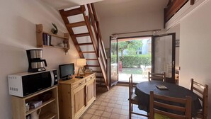 Une cuisine compacte équipée d’un four à micro-ondes, d’une cuisinière et d’une petite table à manger avec des chaises. Une échelle en bois mène à un balcon offrant une vue sur l’extérieur.