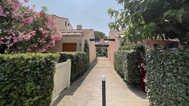 Un chemin menant à un bâtiment doté d’un toit en tuiles, entouré d’une végétation luxuriante et de plantes en fleurs.