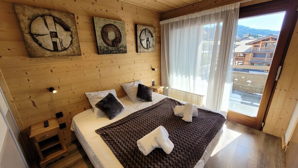 Una habitación con paneles de madera, una cama, una mesita de noche, una ventana con cortinas y obras de arte en la pared.
