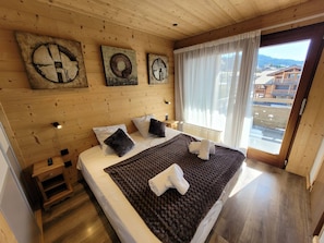 Quarto com painéis de madeira, uma cama, uma mesa de cabeceira, uma janela com cortinas e obras de arte na parede.