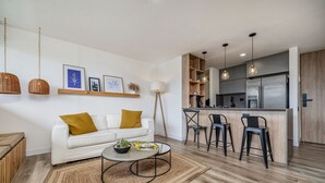 Uma sala de estar moderna com um sofá branco, uma mesa de centro e uma área de cozinha com balcão e banquetas.