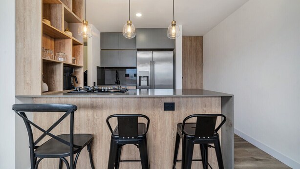 Uma cozinha moderna com ilha central, duas luminárias pendentes e uma estante embutida.