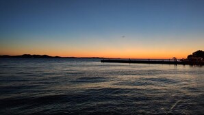 A waterfront scene with a pier extending into calm waters, a distant shoreline, and a clear sky. - Beautiful apartment 100 meters from the lake! (Annecy)