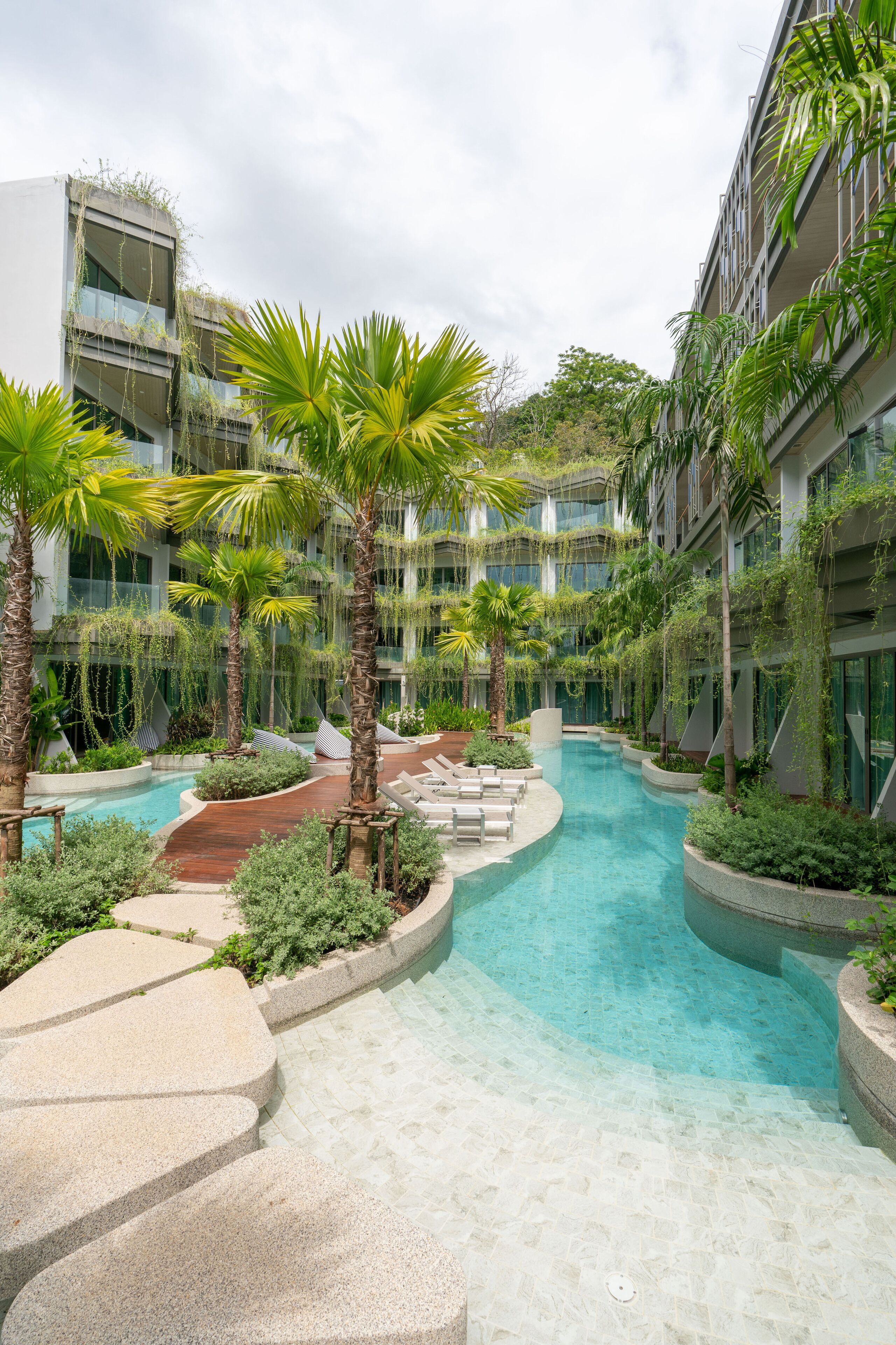 A modern hotel atrium with a central pool, surrounded by lush greenery and palm trees.