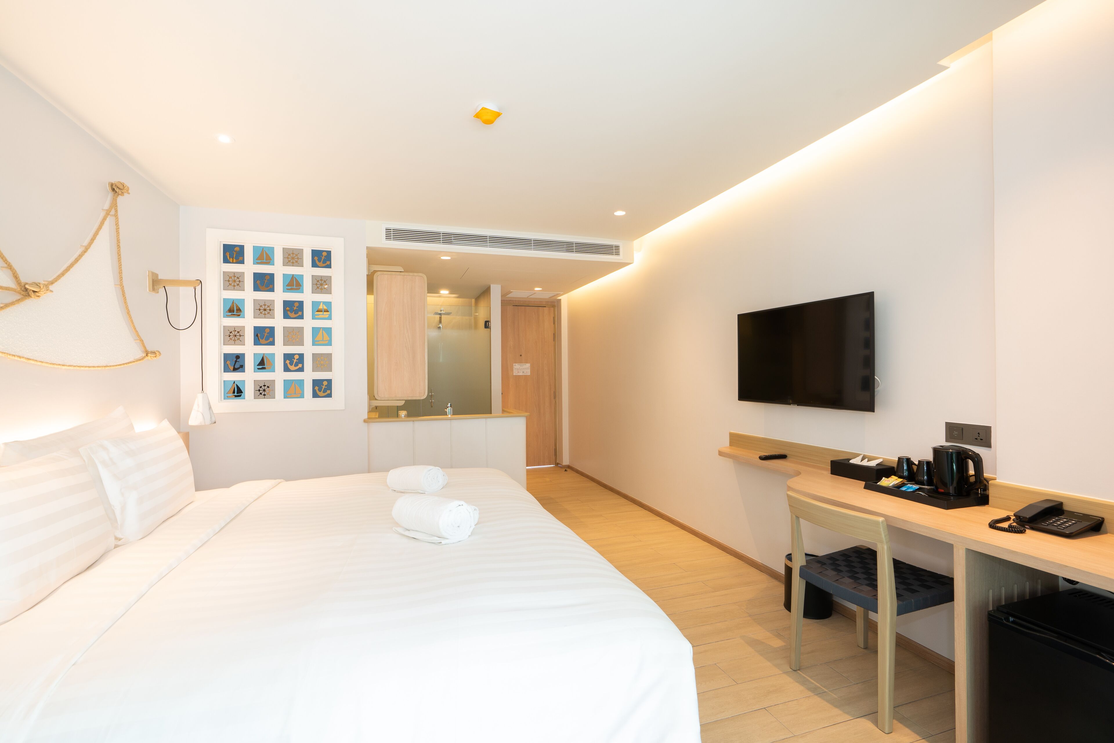 Una habitació d'hotel amb un llit, un escriptori, una televisió i un bany visible a través d'una porta oberta.