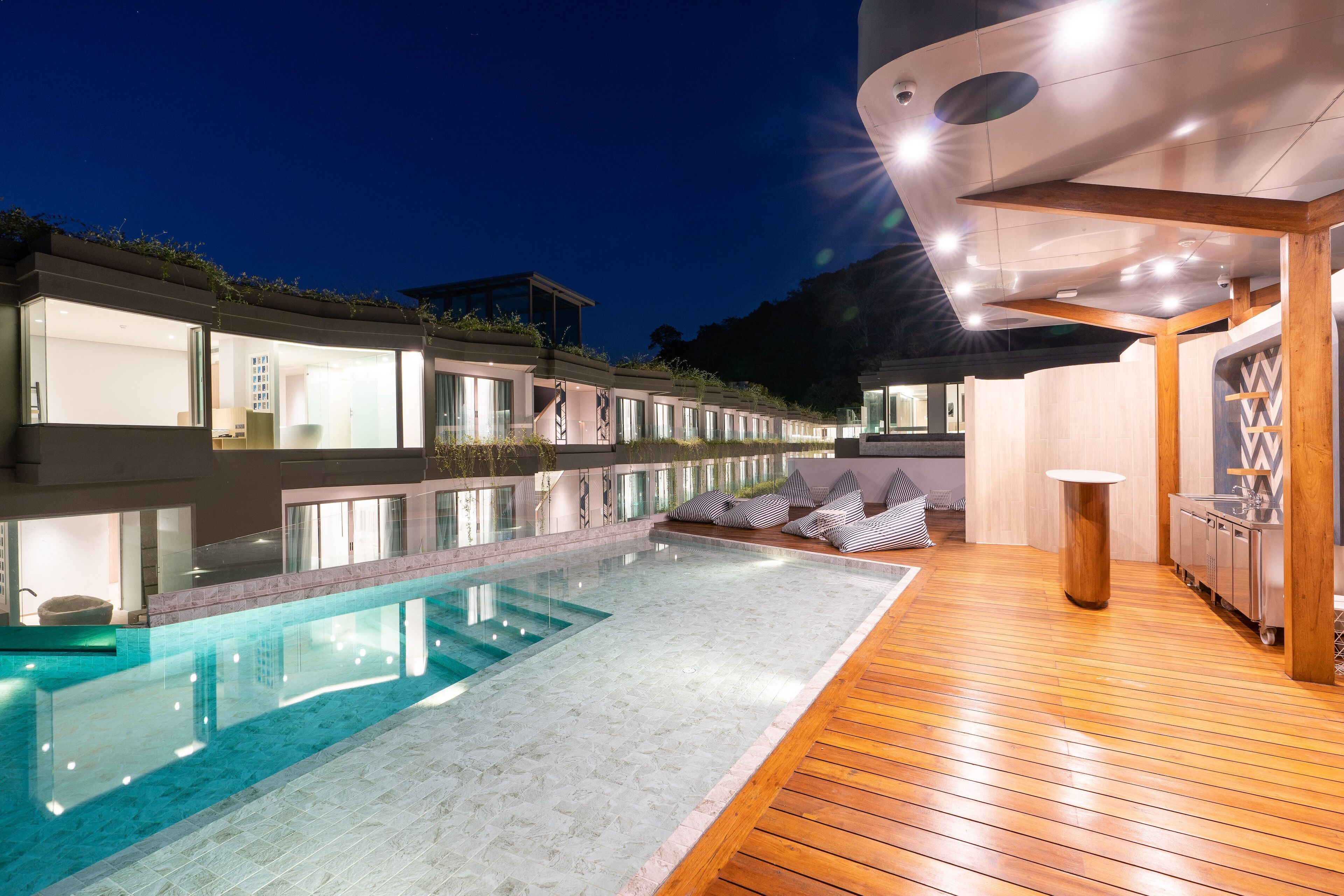 Un hôtel moderne doté d’une piscine, d’une terrasse en bois et de chambres entièrement vitrées.