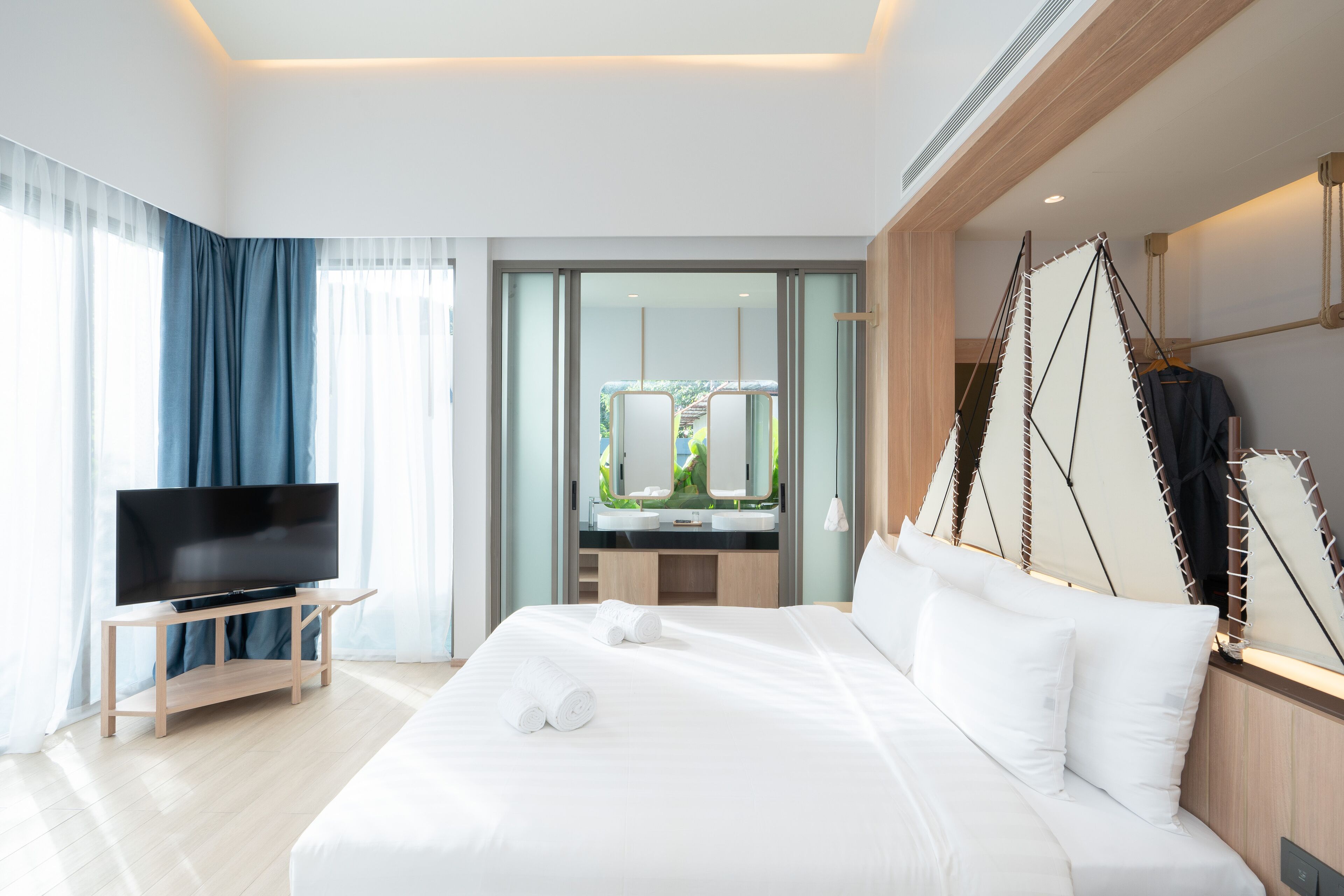 A modern hotel room with a large bed, a flat-screen TV, and a view of a garden through a glass door.