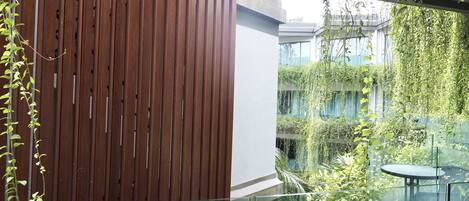 Un edificio moderno con un muro de listones de madera y un balcón de vidrio con vistas a un jardín exuberante.