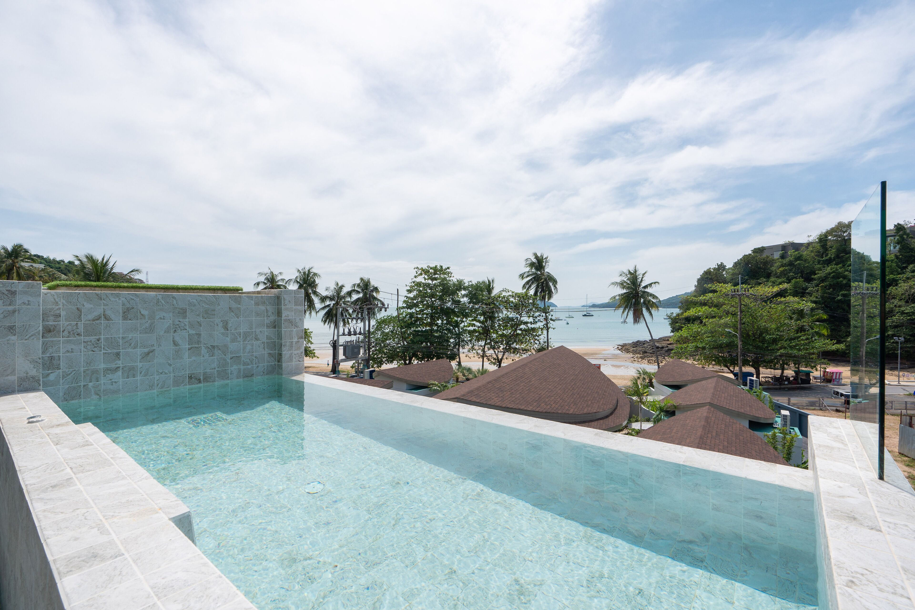 A clear swimming pool with a view of the beach and palm trees.