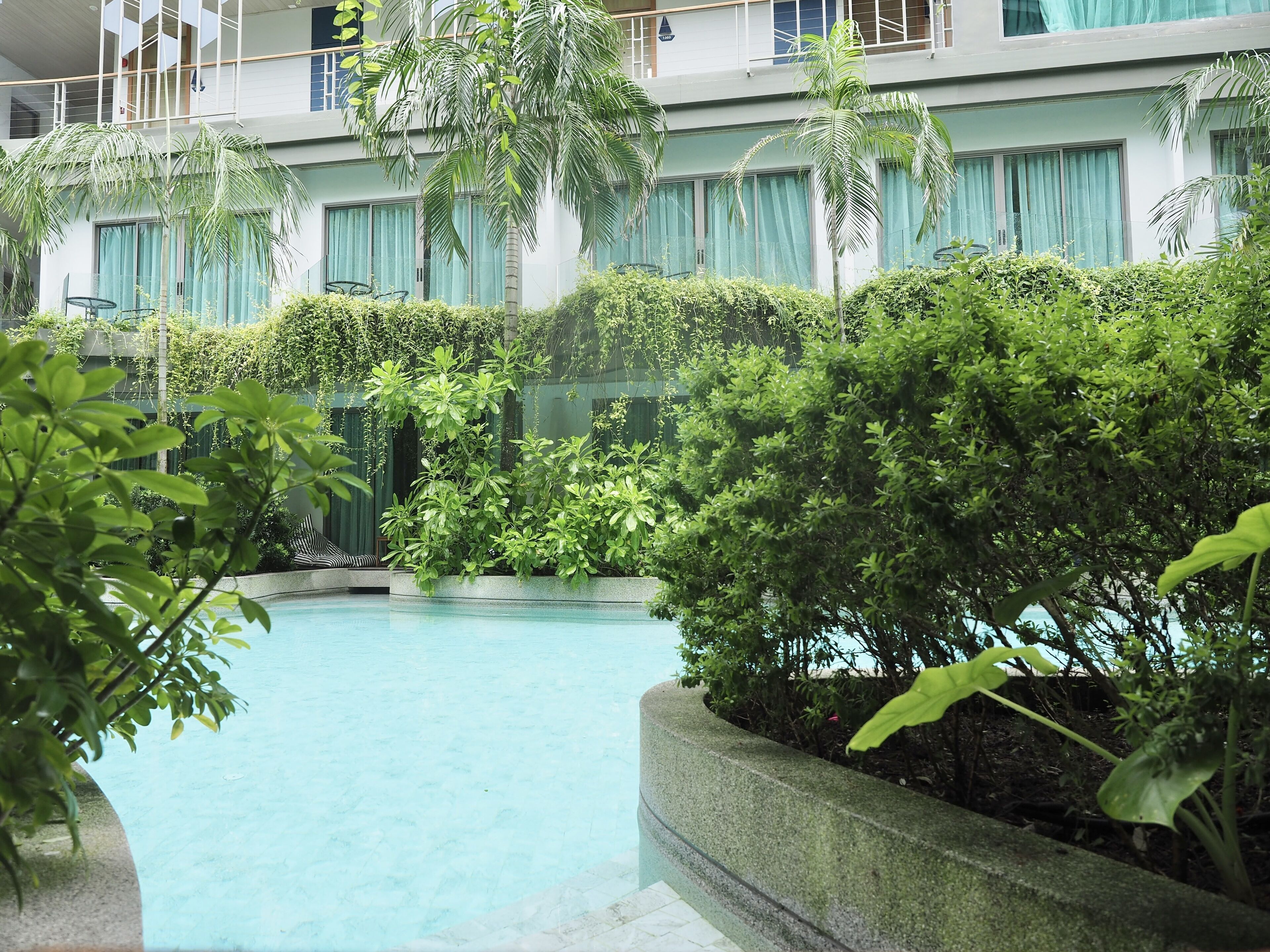 Une piscine entourée d’une végétation luxuriante et un bâtiment doté de nombreux balcons.