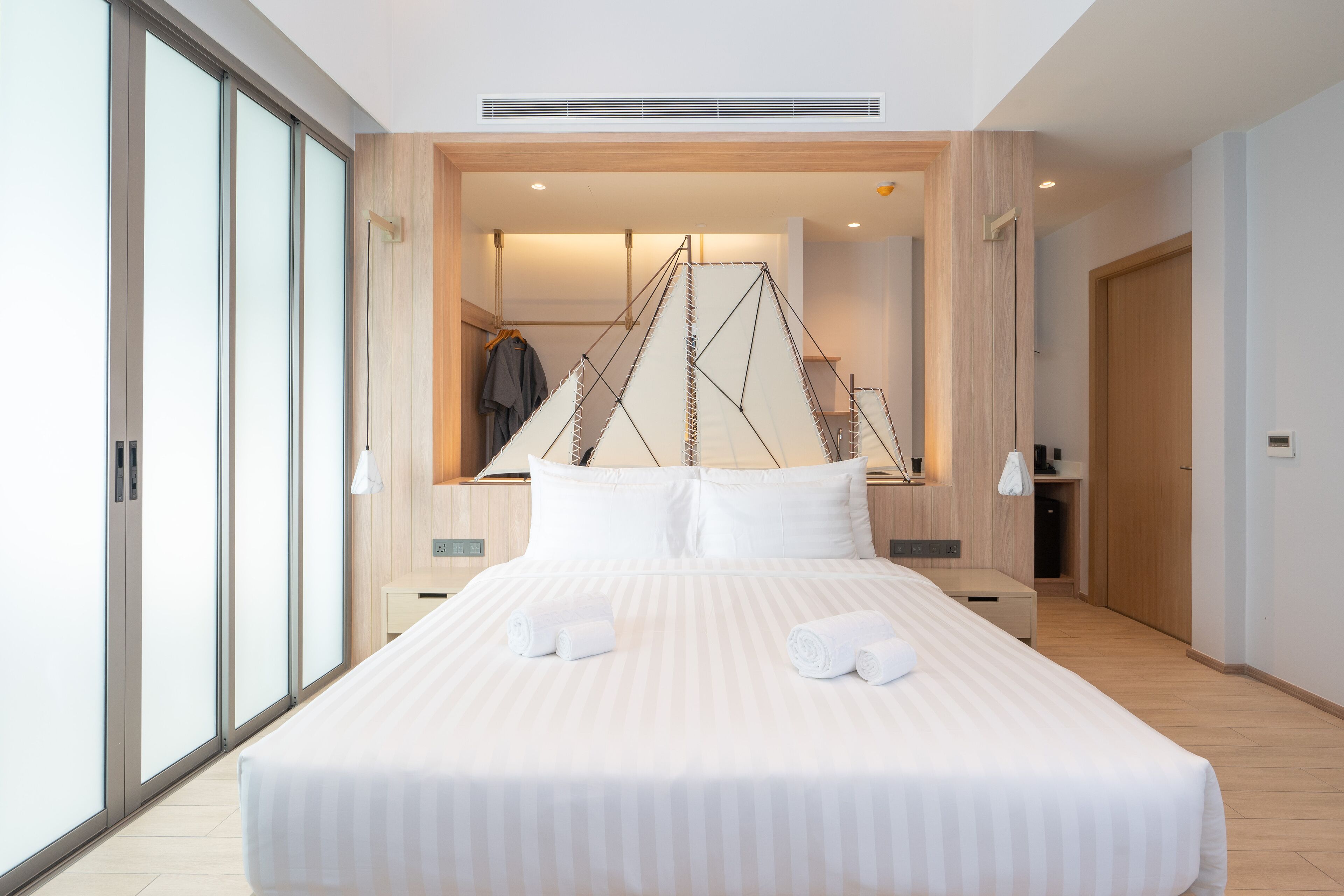 A modern hotel room with a large bed, a wooden headboard, and a large window.
