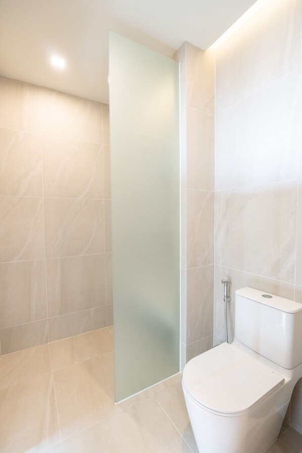 A modern bathroom with a glass shower enclosure, a white toilet, and light-colored tiled walls. - Panwaburi Beachfront Resort (Wichit)