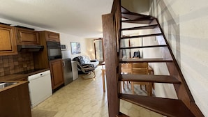 Una cocina con armarios de madera, lavavajillas y microondas. Hay una escalera que conduce a un comedor con sillas y mesa de madera.